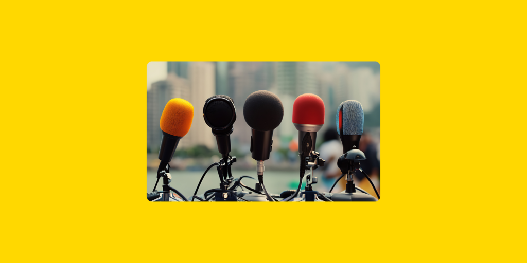 Plusieurs microphones de formes et couleurs variées, alignés au premier plan, avec en arrière-plan des buildings et une vue urbaine.
